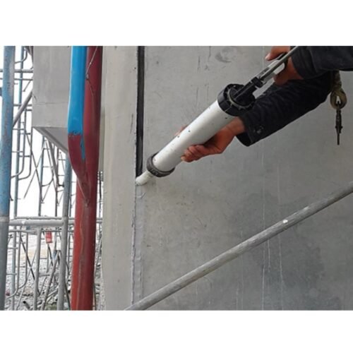A person wearing work clothes is sealing the seams of precast wall blocks outdoors.